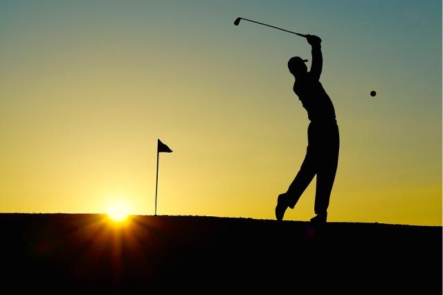 silouette of person swinging a golf club at sunrise